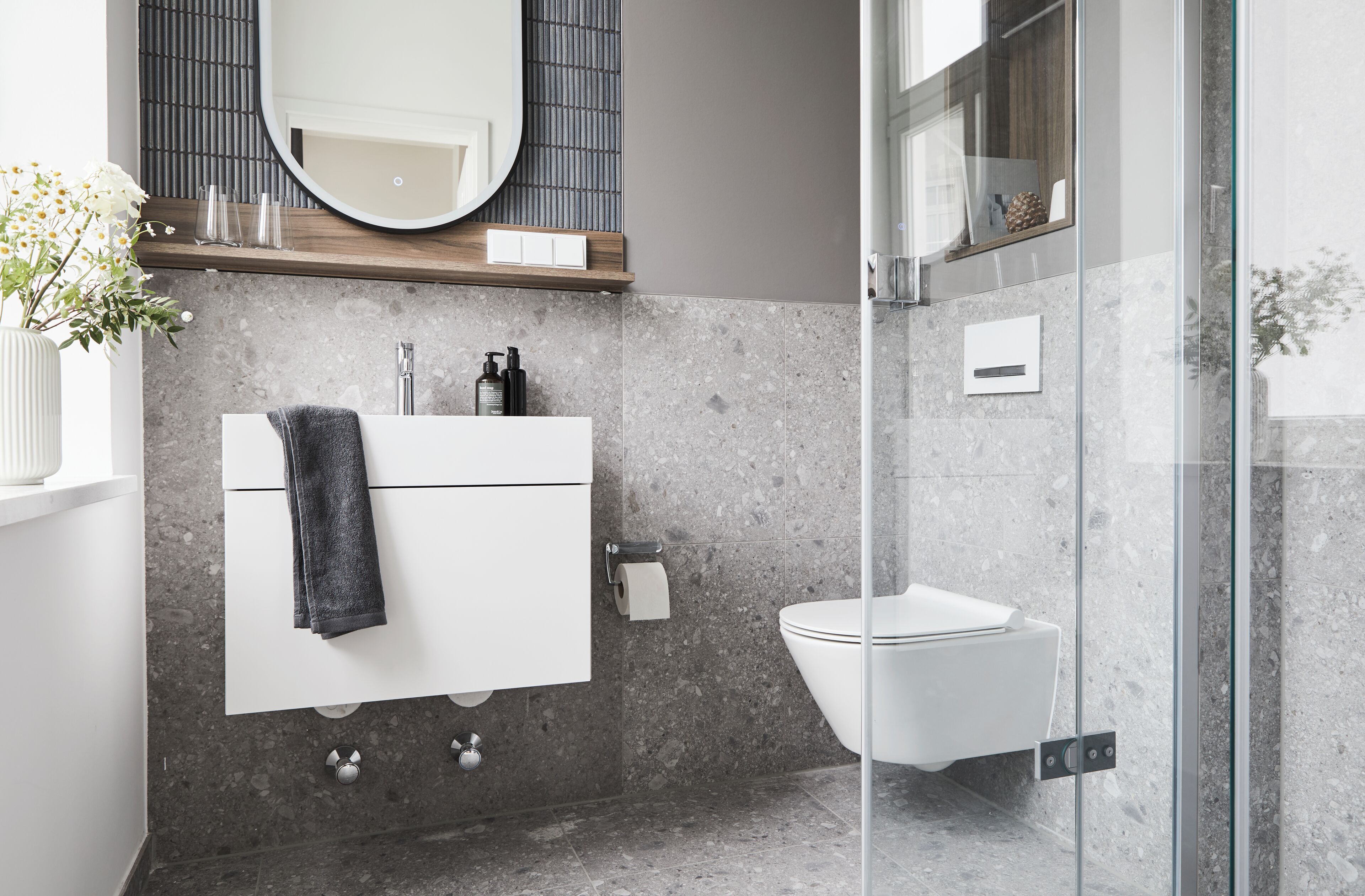 A modern bathroom with a white vanity, a round mirror, and a glass shower enclosure.