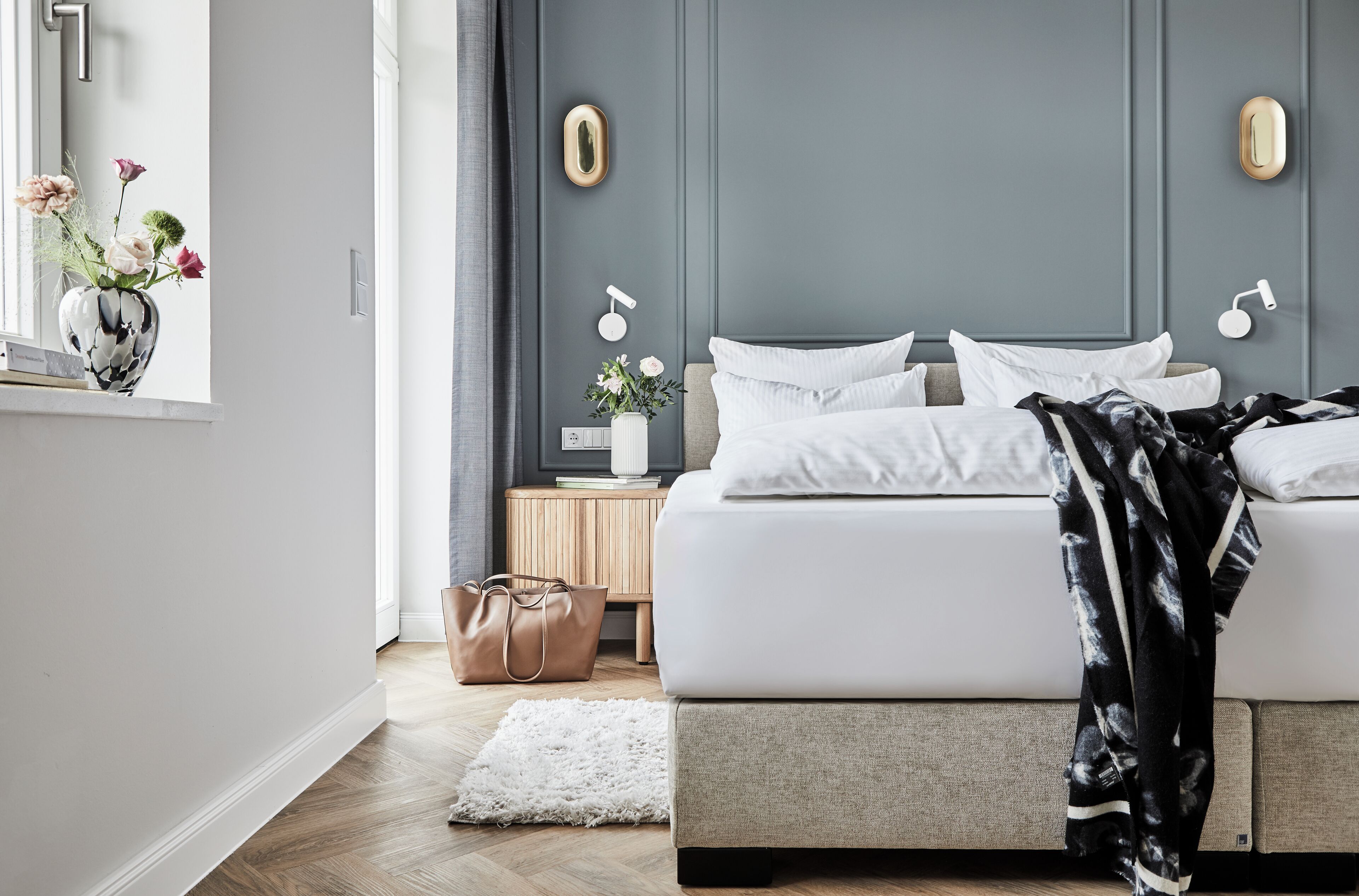 Una camera da letto moderna con un letto, comodini, una finestra con un vaso di fiori e un lampadario a parete.