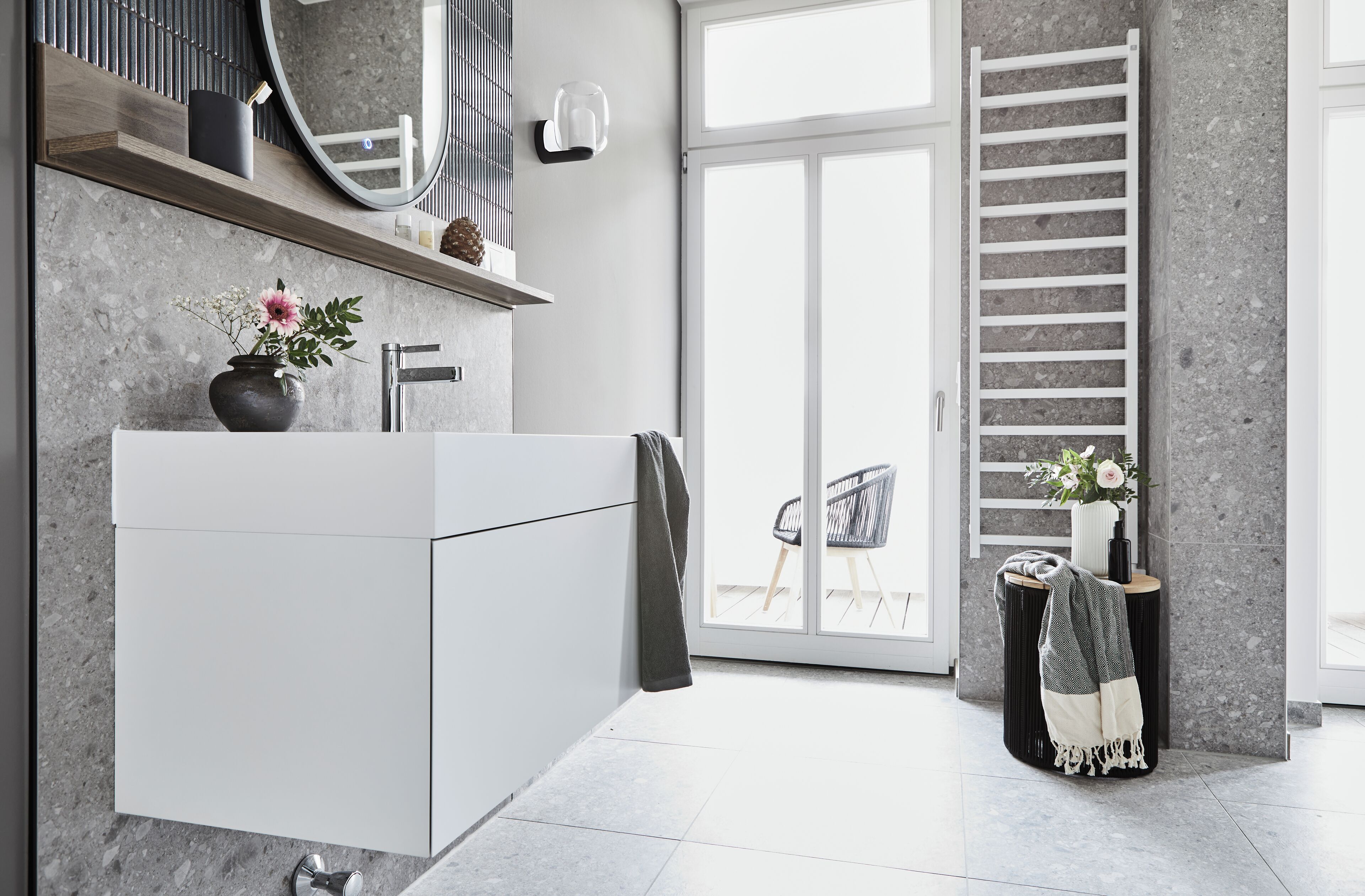 Une salle de bain moderne avec un grand meuble-lavabo blanc, un miroir et un porte-serviettes. On peut voir une plante sur le meuble-lavabo et une serviette suspendue au porte-serviettes.
