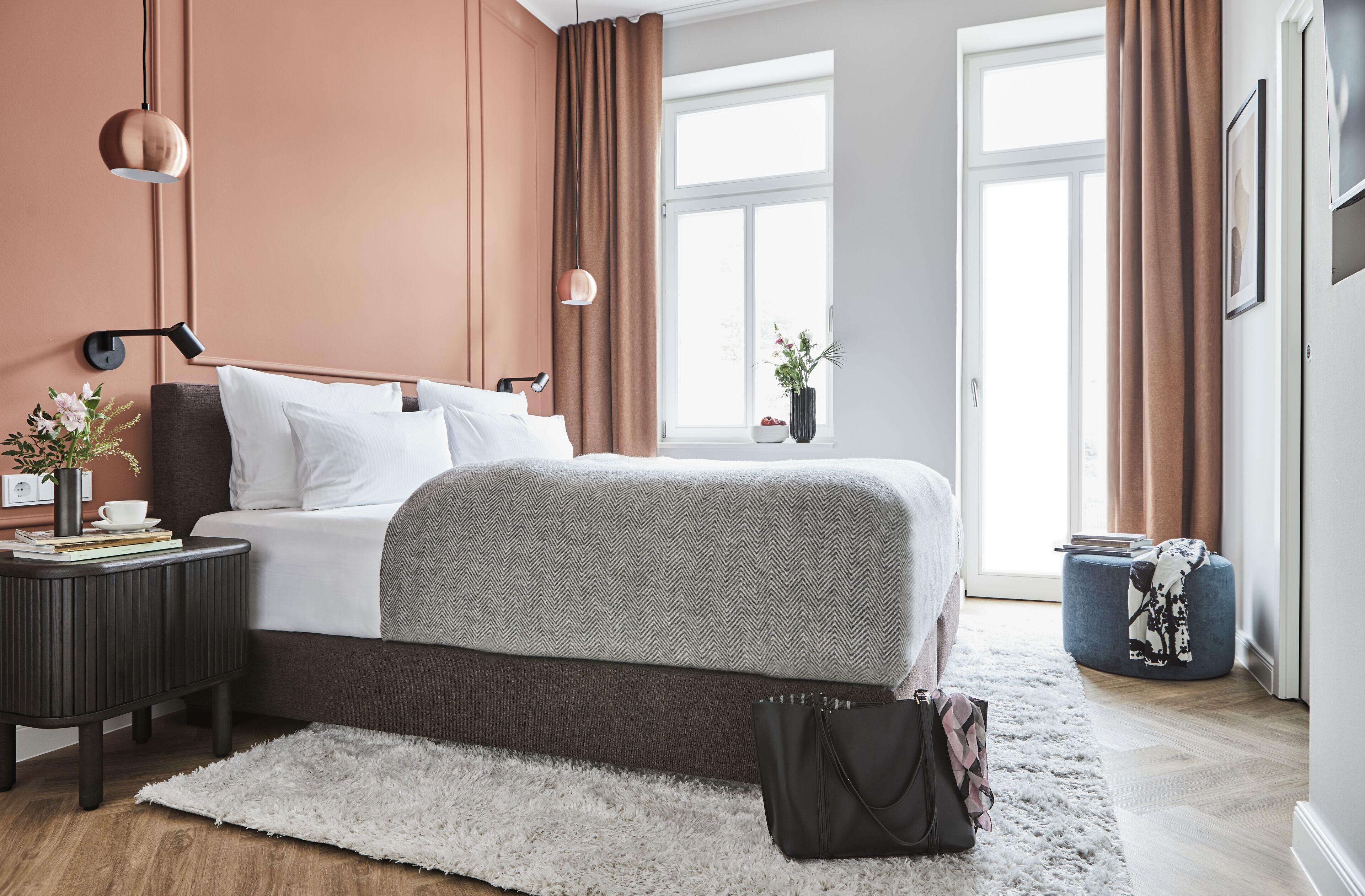 Un dormitorio moderno con cama, mesitas de noche, una ventana grande y vistas al exterior.
