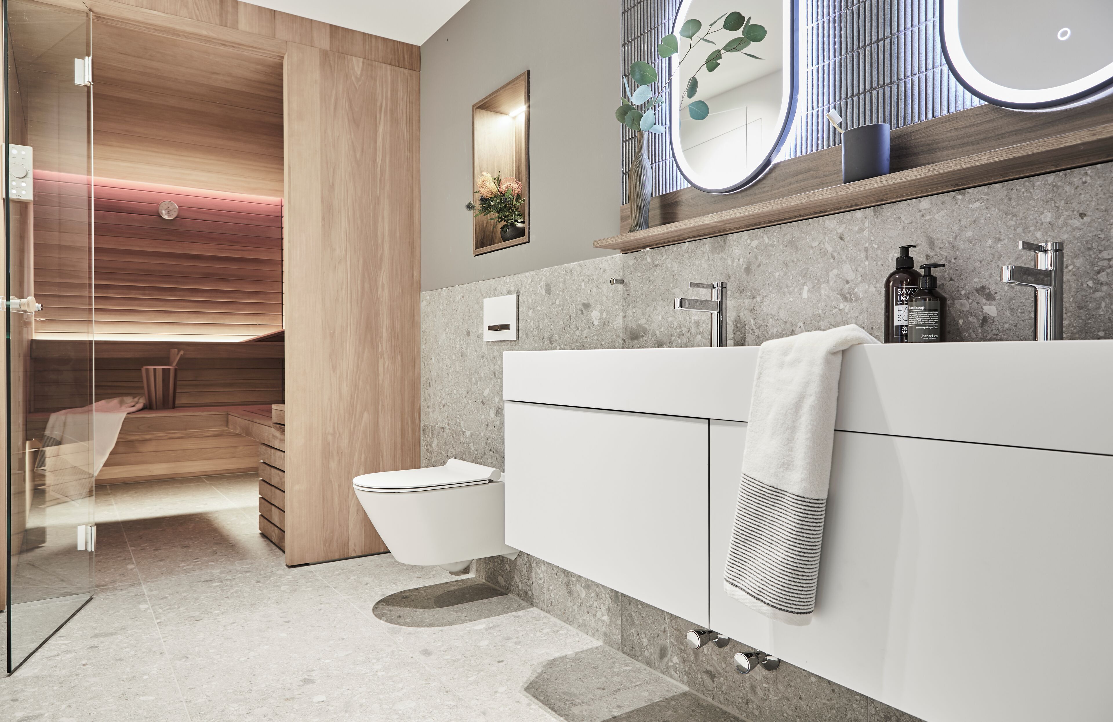 Un baño moderno con cabina de ducha de vidrio, inodoro blanco, espejo grande y tocador empotrado con toallero.