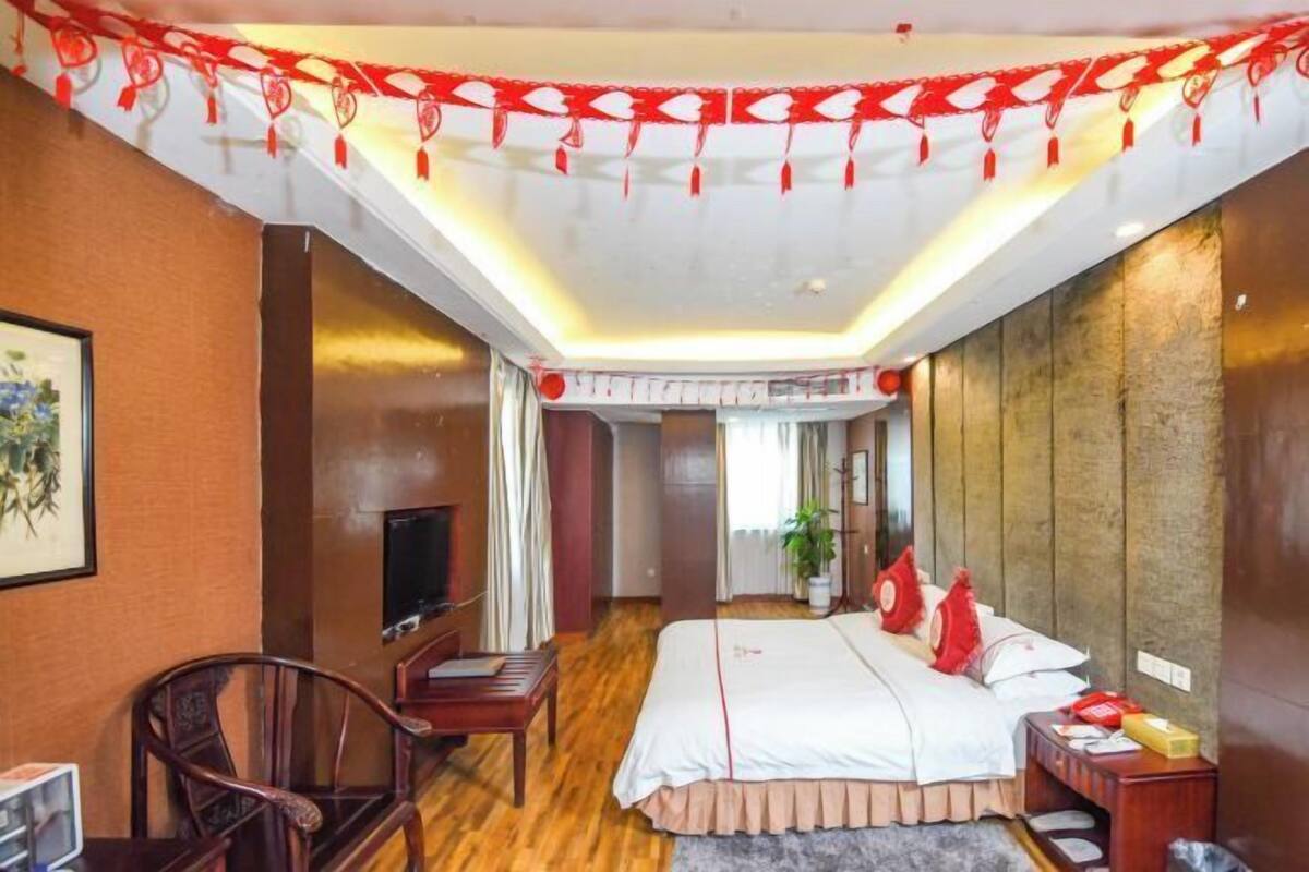 Quarto de hotel com cama, secretária, cadeira, televisão e teto decorativo.
