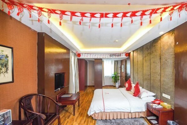 A hotel room with a bed, a TV, a desk, and a chair. - Phoenix Hotel (Xichong)