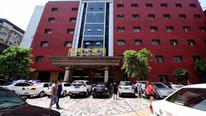 Un edificio de varios pisos con fachada roja, una entrada central y varios coches aparcados delante.
