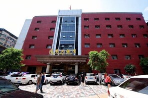 A multi-story building with a red facade, a central entrance, and several parked cars in front. - Phoenix Hotel (Xichong)