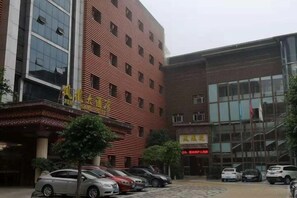 A building with a red brick facade, a modern glass entrance, and several parked cars. - Phoenix Hotel (Xichong)