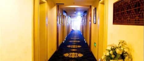 A hotel hallway with a patterned carpet, doors on either side, and a wall-mounted decoration.