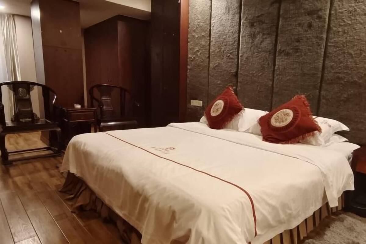 Quarto de hotel com uma cama grande, uma cadeira de madeira e um guarda-roupa de madeira escura.