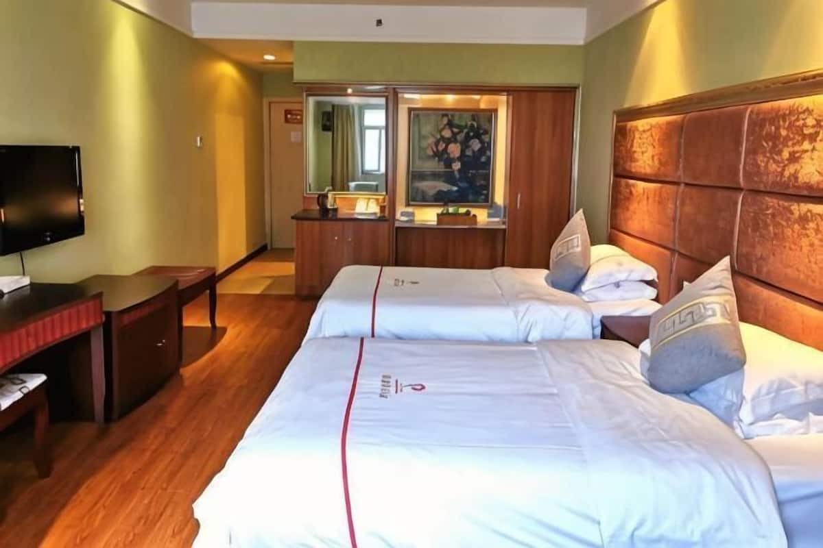Quarto de hotel com cama, escrivaninha, televisão e espelho.