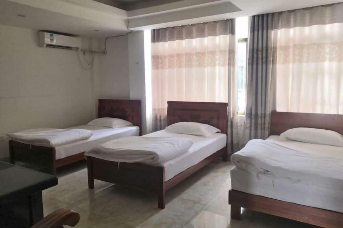Habitación de hotel con dos camas individuales, cabecero de madera, escritorio y unidad de aire acondicionado en la pared.