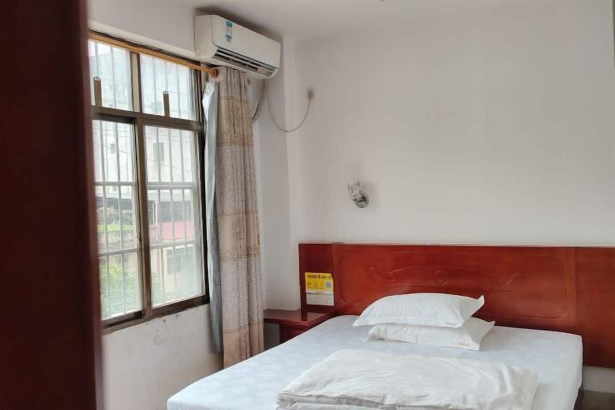 Habitación de hotel con cama, ventana con cortinas, unidad de aire acondicionado y una lámpara fijada a la pared.