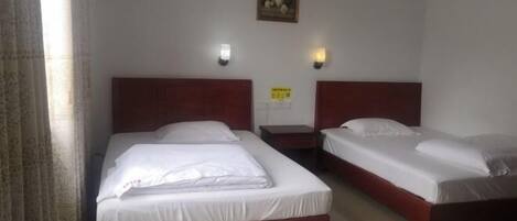A hotel room with two single beds, a nightstand, a wall-mounted light, and a framed picture.