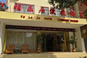 Entrada de hotel con un letrero en idioma extranjero, una puerta y dos plantas en macetas.