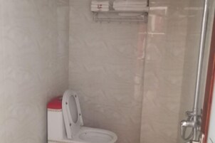 Un pequeño box de ducha cerrado con inodoro, un perchero sobre el inodoro y un cabezal de ducha.