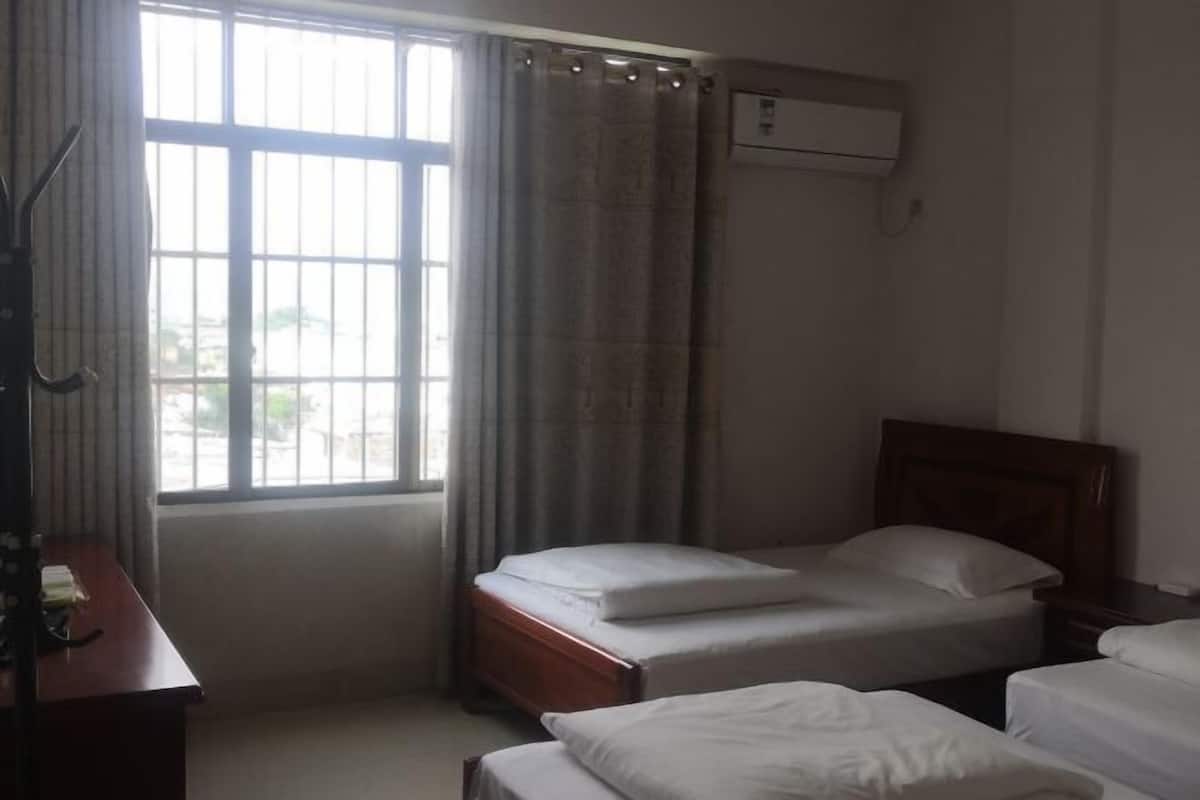 Habitación de hotel con dos camas individuales, un escritorio y una ventana con cortinas.