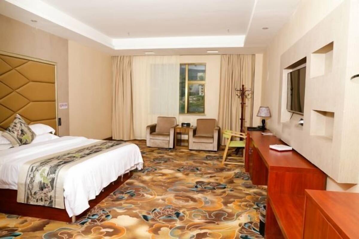 Een hotelkamer met een bed, twee fauteuils, een bureau en een televisie.