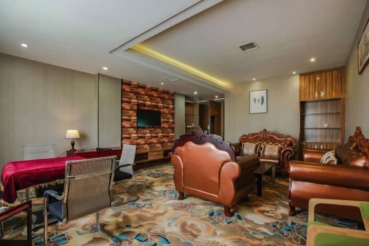 Een hotelkamer met een rood bed, een wand van hout, een leren bank en een kamerbreed tapijt met patroon.