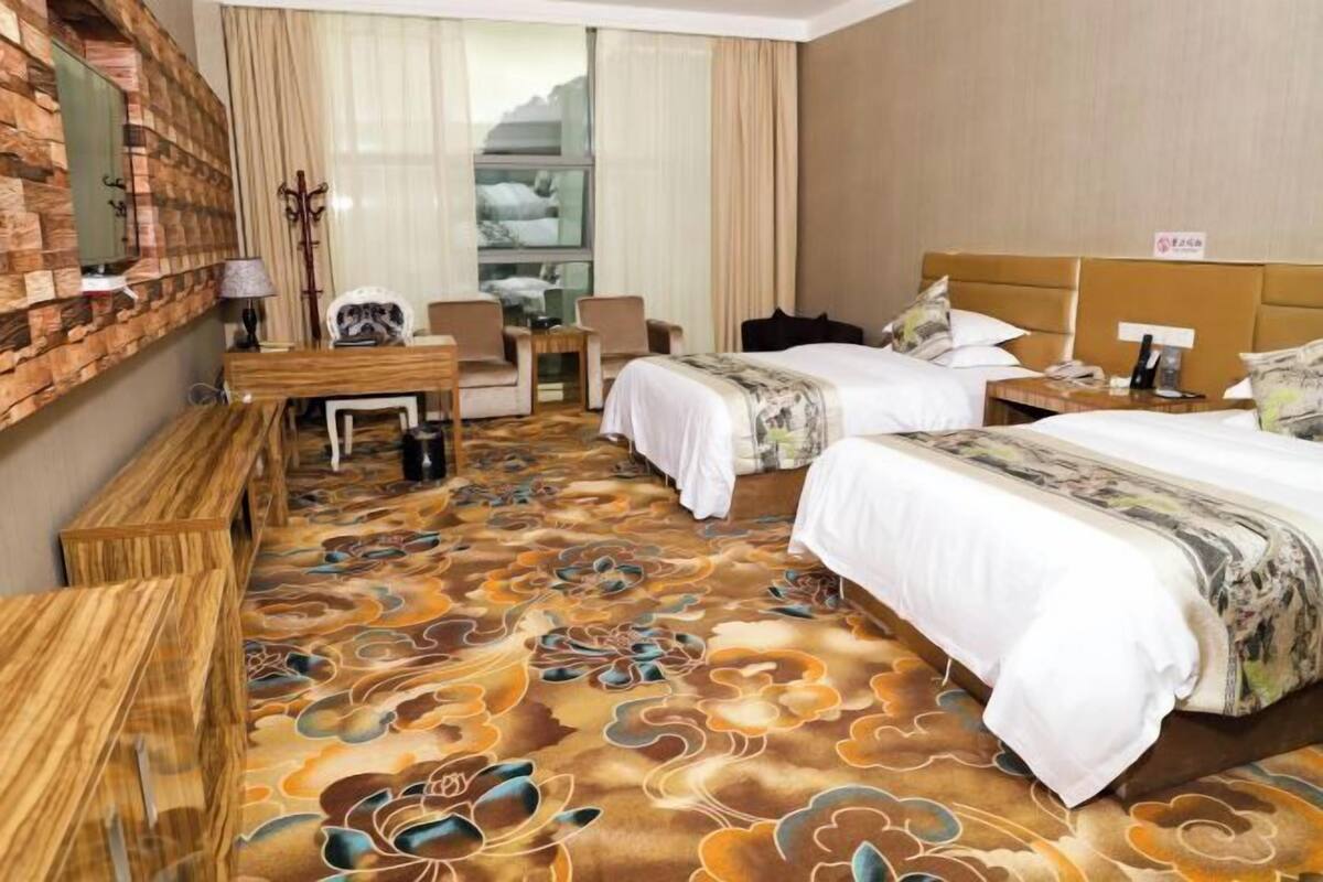 Een hotelkamer met twee bedden, een bureau, een stoel, een televisie en een groot raam.
