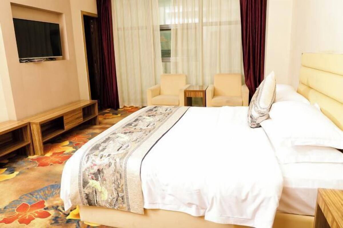 Hotelkamer met een bed, een aan de muur bevestigde televisie, een tafeltje, twee stoelen en een raam met gordijnen.