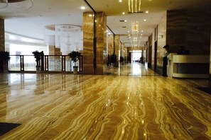 A spacious lobby with a polished marble floor, a reception desk, and a modern chandelier.
