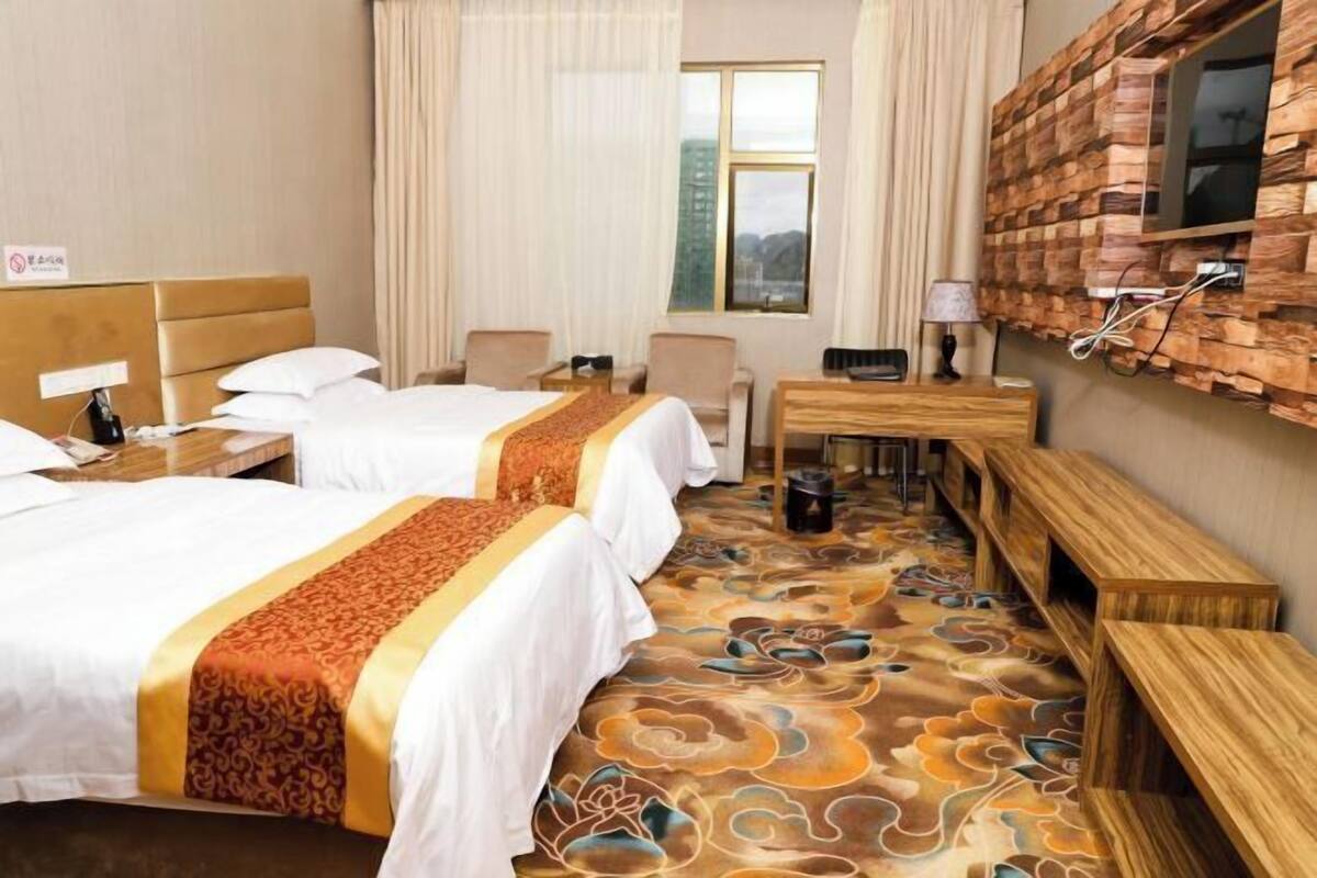 Hotelkamer met twee bedden, een bureau, stoelen, een televisie bevestigd aan een houten wand en een kamerbreed tapijt met een patroon.