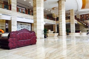 Un vestíbulo amplio con suelo de mármol, una imponente escalera y una zona de estar con un sofá estampado.