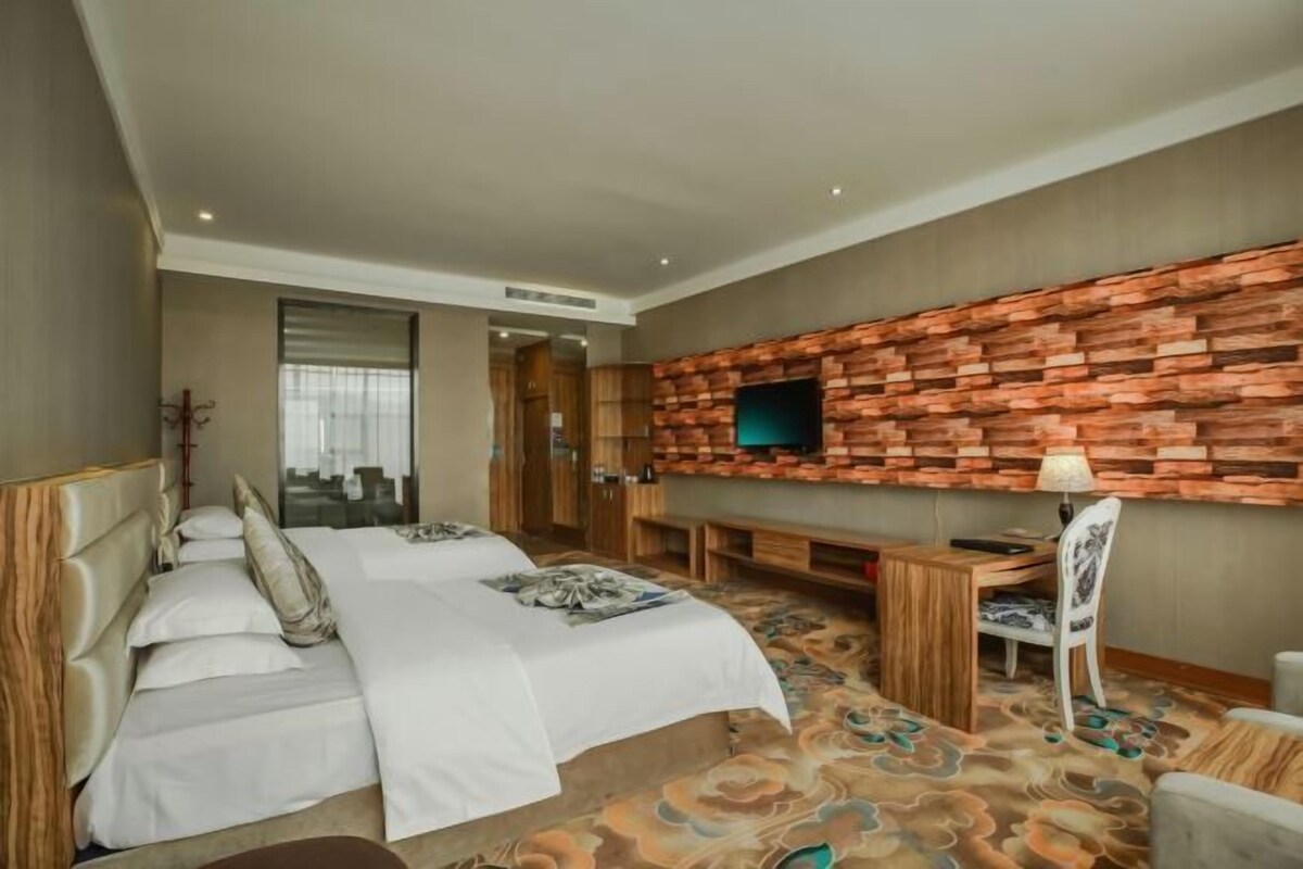 Ein Hotelzimmer mit Bett, Schreibtisch, Stuhl, Fernseher an einer Ziegelwand und einem gemusterten Teppich.