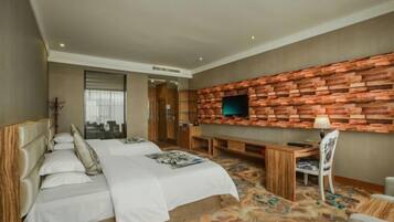 A hotel room with a bed, a desk, a chair, a TV mounted on a brick wall, and a patterned carpet.