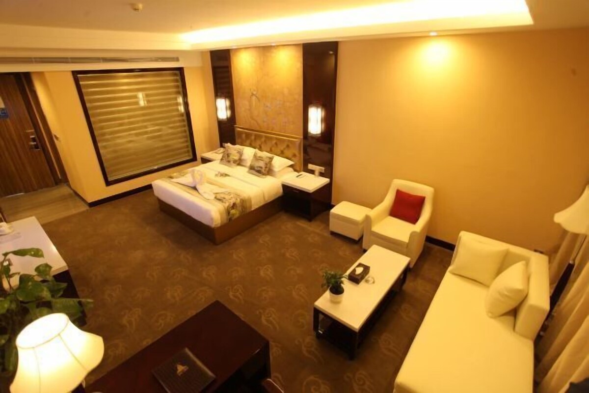 Ein Hotelzimmer mit einem großen Bett, zwei weißen Sesseln, einem kleinen Sofa, einem Couchtisch und einem Schreibtisch mit Lampe.