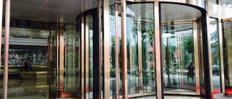 A revolving door with glass panels, a red carpet, and a marble floor.