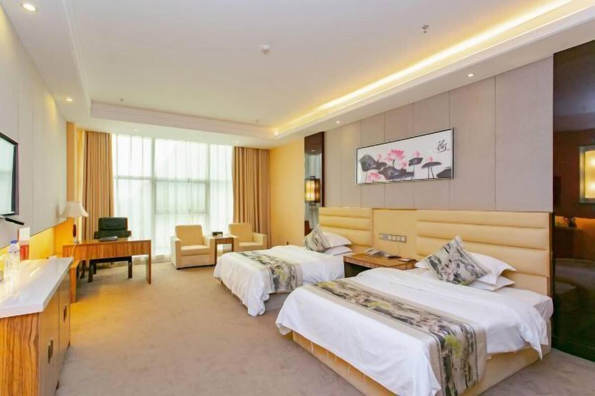 Een hotelkamer met twee bedden, een bureau, een stoel, een televisie en een groot raam.