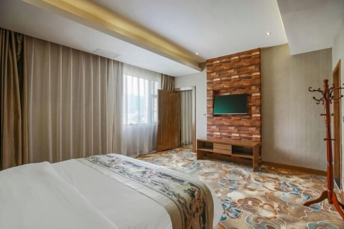 Ein Hotelzimmer mit Bett, Vorhängen, einer Holzwand mit Fernseher und einem gemusterten Teppich.