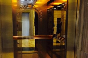 Interior de un ascensor con paredes metálicas y un pasamanos.