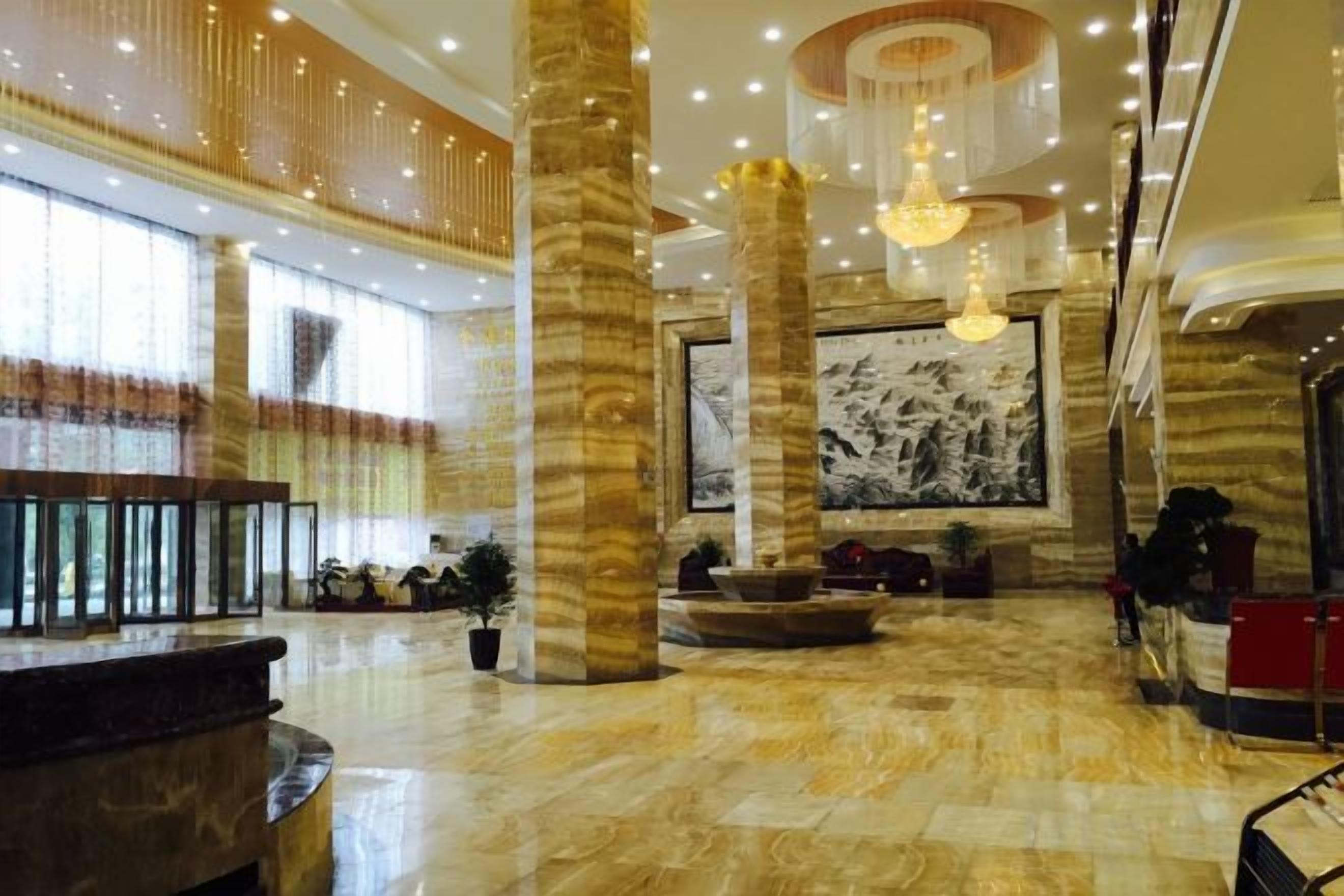 A spacious lobby with marble flooring, large columns, a reception desk, and a large wall-mounted artwork.