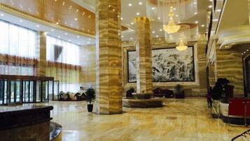 A spacious lobby with marble flooring, large columns, a reception desk, and a large wall-mounted artwork.