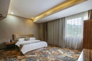 Una habitación de hotel con cama, mesita de noche, ventana con cortinas y vistas al exterior.