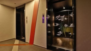 A hallway with two elevators, one with a digital display and another with a red accent wall. - Orange Hotel (Hefei Huaihe Road Pedestrian Street Dadongmen Metro Station) (Hefei)