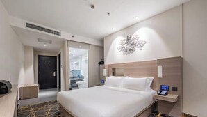A modern hotel room with a large bed, a bedside table with a phone, and a wall-mounted light fixture. - Orange Hotel (Hefei Huaihe Road Pedestrian Street Dadongmen Metro Station) (Hefei)
