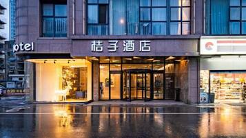 Entrada de un hotel con puerta de cristal, un cartel sobre la puerta y un reflejo en el suelo mojado.