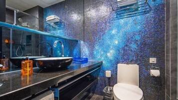 Un baño moderno con pared de mosaicos, encimera negra, inodoro blanco y un espejo.