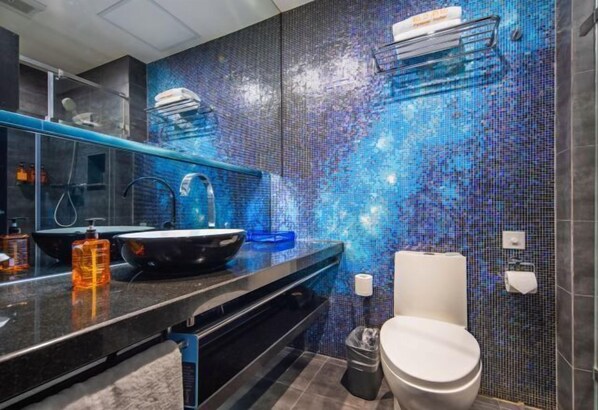 Um banheiro moderno com parede de mosaico, bancada preta, vaso sanitário branco e espelho.