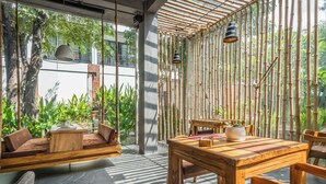 A modern outdoor seating area with a wooden table and chairs, surrounded by bamboo walls and large windows. - Bamboo Retreat Villa (Siem Reap)