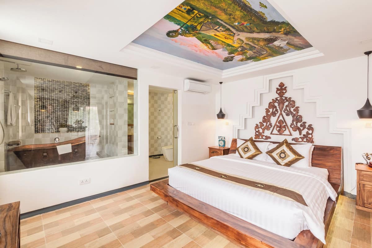 A bedroom with a large bed, a wooden headboard, a ceiling mural, and a large mirror.