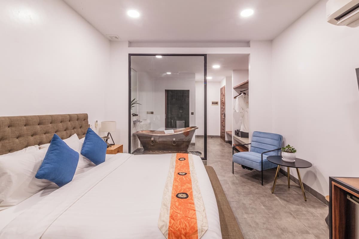 A modern hotel room with a large bed, a blue chair, a small table, and a unique bathtub.