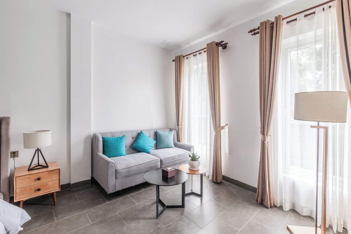 A modern living room with a grey sofa, teal cushions, a small round table, a lamp, and curtains.
