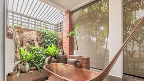 A spa area with a copper bathtub, a brick wall with greenery, and a large window with a view of trees. - Bamboo Retreat Villa (Siem Reap)