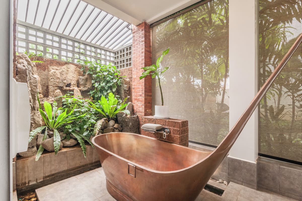 A spa area with a copper bathtub, a brick wall with greenery, and a large window with a view of trees.