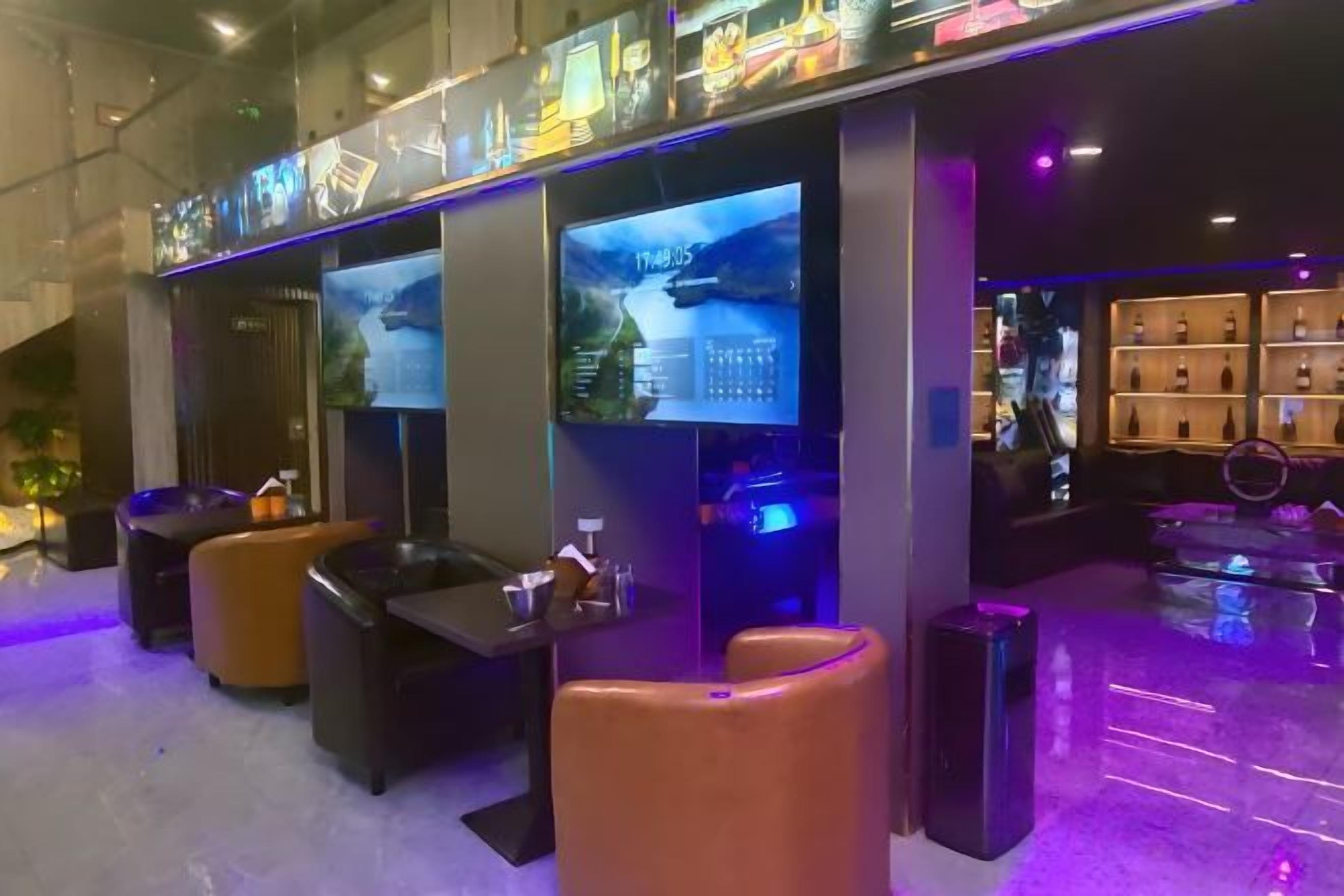 A modern hotel lobby with seating areas, a reception desk, and large digital displays.