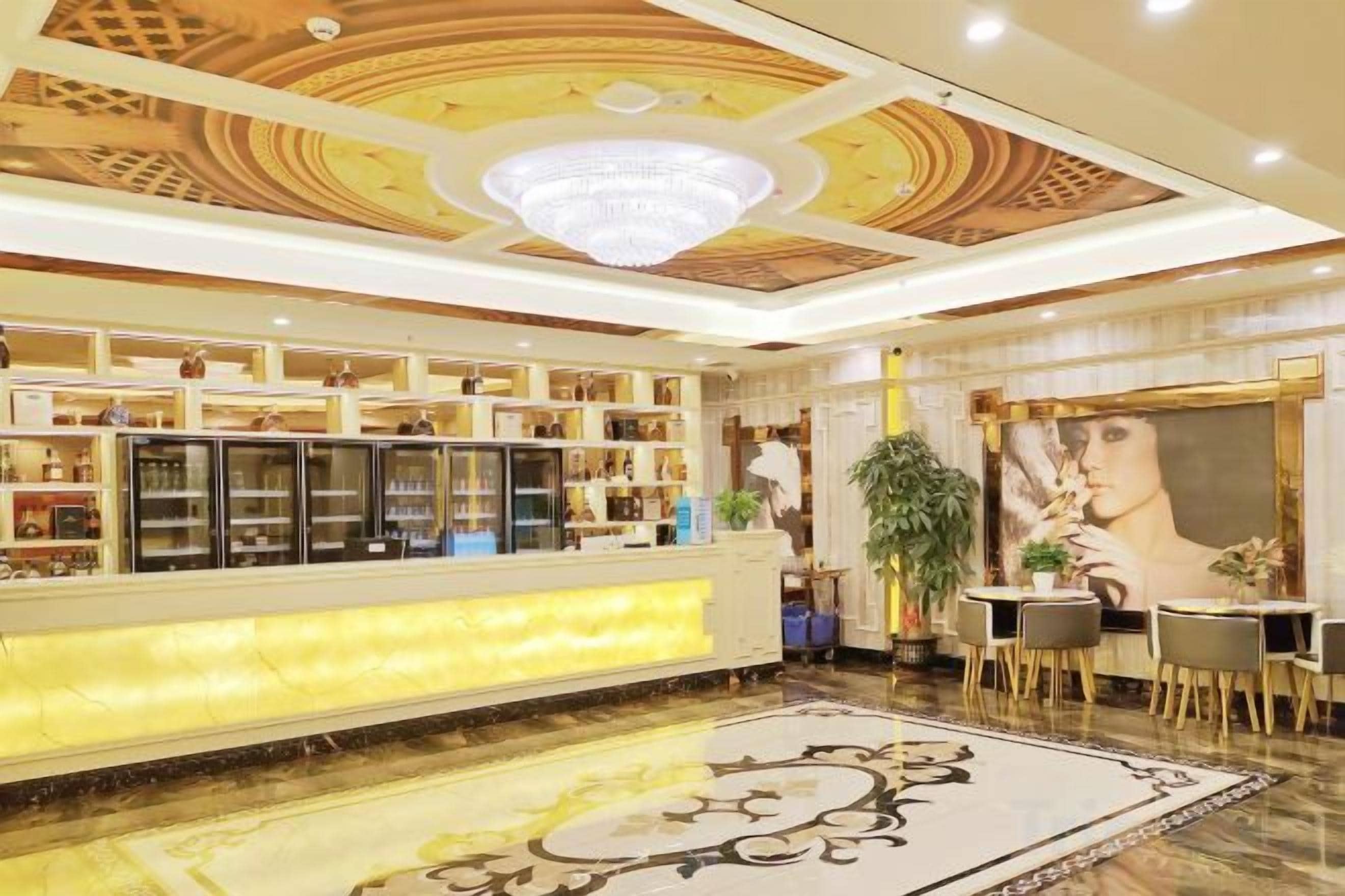 A hotel lobby with a reception desk, a chandelier, a large painting, and a patterned carpet.
