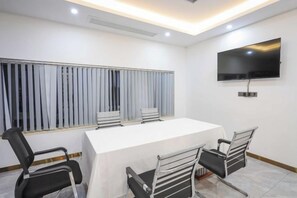 A conference room with a long table, four chairs, a TV on the wall, and blinds on the window. - Licheng Hotel (Zhongshan Xiaolan High-speed Railway Dongsheng Station Branch) (Zhongshan)